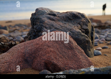Schließen Sie herauf Bild von zwei großen Steinen auf einem sandigen und steinigen Strand mit einer menschlichen Figur am Ufer in der Ferne Stockfoto