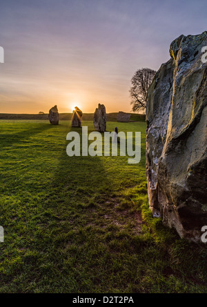 Die Sonne geht hinter Teil des großen Steinkreises in Avebury, Wiltshire, UK lange Schatten über den Boden. Stockfoto