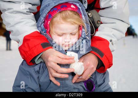 Mutter / Mutter gilt / Sonnencreme für das Gesicht der Tochter junge Kleinkind während auf einer sonnigen Höhenlage Skipiste anwenden. Stockfoto