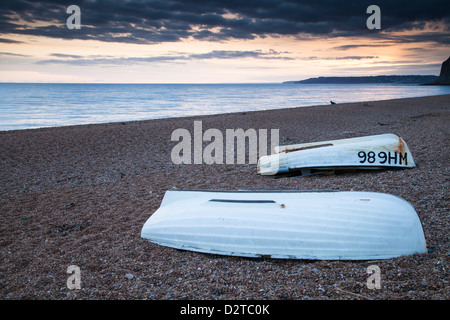 Ein paar der umgedrehten hölzerne Fischerboote auf einladendstens Kiesstrand bei Sonnenuntergang über Lyme Regis und Lyme-Bucht an der Jurassic Coast, Dorset, England Stockfoto