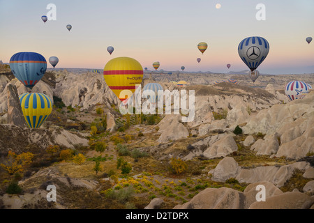 Viele Heißluftballons über das Rote Tal mit Höhle Kirchen Kappadokien Göreme Nationalpark Nevsehir Türkei in der Morgendämmerung mit Mond Stockfoto