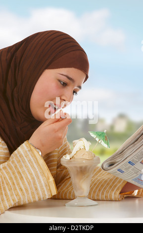 Junge verschleierte Frau eine Zeitung lesen und Essen ein Eis (keine Markennamen kann gelesen werden) Stockfoto