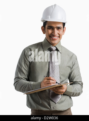 Porträt eines männlichen Ingenieur tragen Helm und schreiben auf einem Klemmbrett Stockfoto