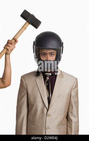 Person die Hand, die Kollision mit eines Hammers auf einen Geschäftsmann, einen Helm zu tragen Stockfoto