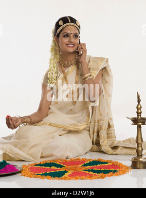 Indische Frau in traditioneller Kleidung machen Rangoli und telefonieren mit einem Handy Stockfoto
