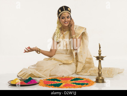 Indische Frau in traditioneller Kleidung machen Rangoli und telefonieren mit einem Handy Stockfoto