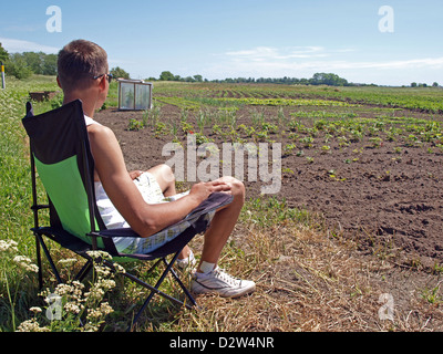 Junglandwirt sitzen in klappbarer Sessel und auf seinen Feldern Stockfoto