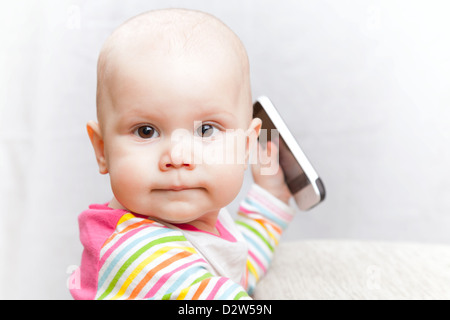 Kleines Baby in bunt gestreiften Freizeitkleidung spielt mit Handy Stockfoto