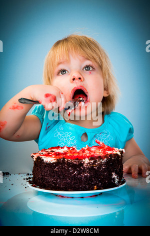 Kleines Mädchen essen Kuchen auf blauem Hintergrund Stockfoto