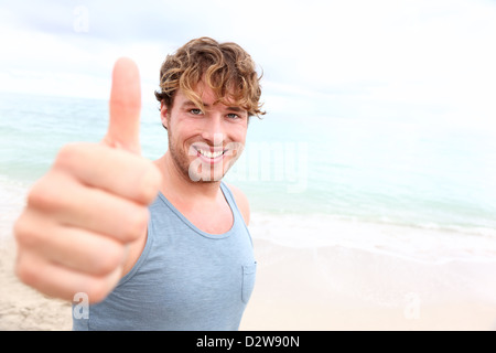 Porträt von glücklich gut aussehender Mann geben Daumen nach oben Erfolg Zeichen beim Training draußen am Strand Stockfoto