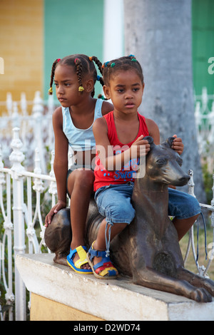 zwei junge Mädchen sitzen auf ornamentalen Hund auf Platz in Trinidad, Kuba, Westindische Inseln, Karibik, Mittelamerika im März Stockfoto