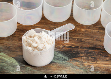 Kugel von Molke-Protein-Pulver auf einer Holzfläche umgeben von leeren Kunststoff Schaufeln Stockfoto