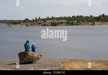 Karlskrona, Schweden, Kinder sitzen auf einem Felsen am Ufer und Blick auf die Ostsee Stockfoto