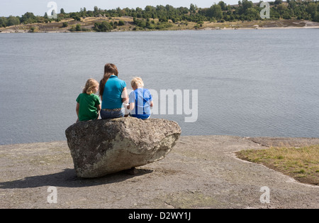Karlskrona, Schweden, Kinder sitzen auf einem Felsen am Ufer und Blick auf die Ostsee Stockfoto