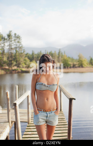 Frau blickte mit Hände in den Taschen auf Dock über See Stockfoto