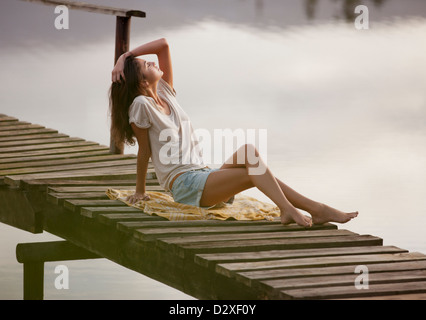 Frau mit Kopf in den Nacken und Hand im Haar auf Dock über See Stockfoto