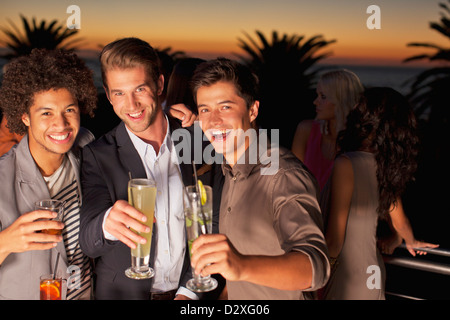 Porträt des Lächelns Männer Toasten Cocktails am Balkon bei Sonnenuntergang Stockfoto