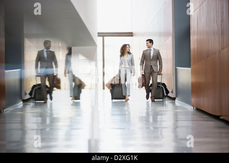 Unternehmer und Unternehmerin ziehen Koffer durch Korridor Stockfoto