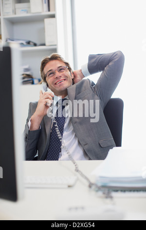 Lächelnde Geschäftsmann am Schreibtisch im Büro am Telefon sprechen Stockfoto