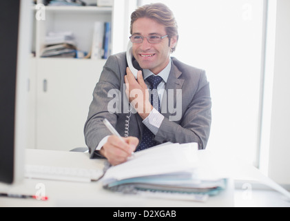Lächelnde Geschäftsmann am Telefon sprechen und schreiben Stockfoto