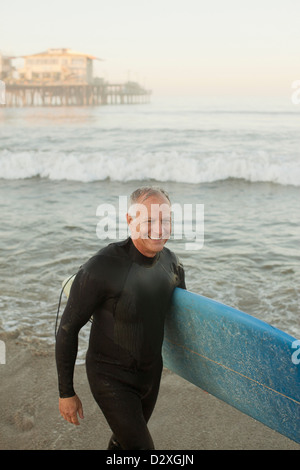 Ältere Surfer tragen Board am Strand Stockfoto