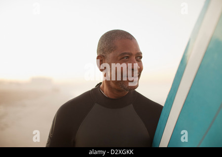 Ältere Surfer tragen Board am Strand Stockfoto