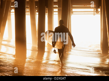 Ältere Surfer tragen Board unter pier Stockfoto