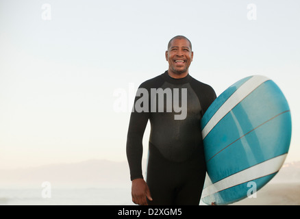 Ältere Surfer tragen Board am Strand Stockfoto