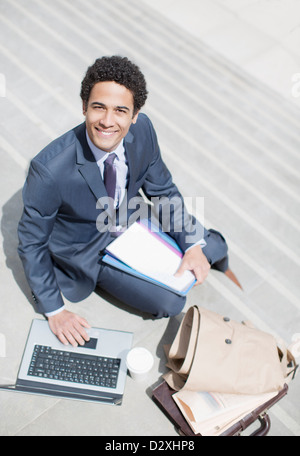 Porträt von lächelnden Geschäftsmann mit Papierkram mit Laptop auf sonnigen Treppe Stockfoto