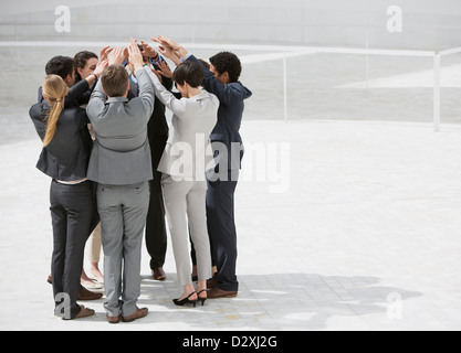 Geschäftsleuten stehen im Huddle mit erhobenen Armen Stockfoto