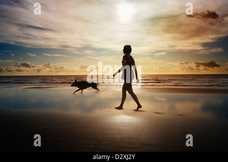 Silhouette der Frau und Hund am Strand spazieren