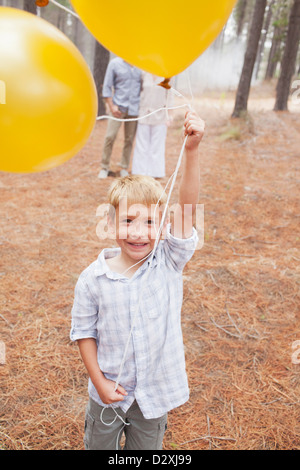 Porträt von lächelnden jungen Holding Ballons in Wäldern mit den Eltern im Hintergrund Stockfoto