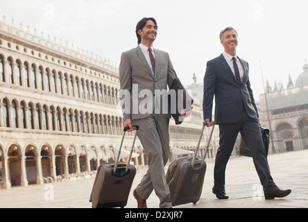 Lächelnde Geschäftsleute zu Fuß mit Koffern durch den Markusplatz in Venedig Stockfoto