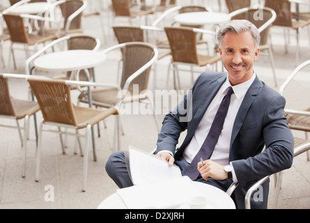 Porträt von lächelnden Geschäftsmann mit Papierkram am Straßencafé Stockfoto