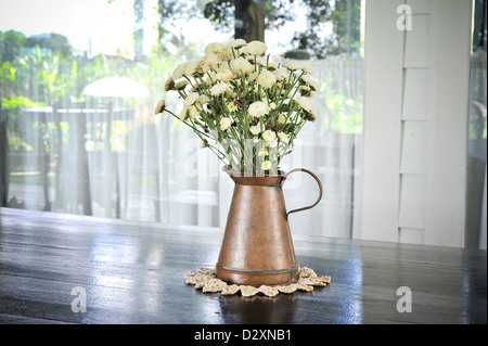 weiße Blume in einem antiken Metall Kanne auf der hölzernen Tischplatte Stockfoto