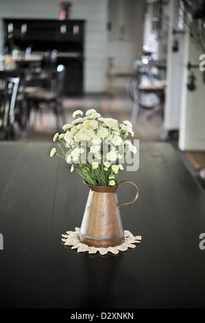 weiße Blume in einer antiken Metall Kanne auf die schwarze hölzerne Tischplatte Stockfoto