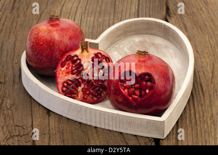 Zwei ganze und halbe Granatapfel auf einem Tablett, Granatapfel mit herzförmigen Ausschnitt Stockfoto