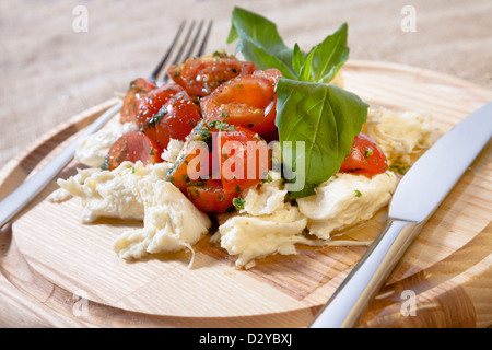 Caprese-Salat auf einer runden hölzernen Schale mit Messer und Gabel Stockfoto