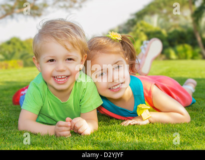 Bild von Bruder und Schwester, die Spaß im Park, zwei fröhliche Kind Festlegung auf grünen Rasen, kleine Mädchen und Jungen spielen Stockfoto