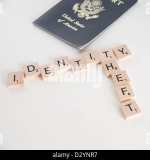 Identitätsdiebstahl geschrieben in Scrabble Buchstaben mit US-Pass im Hintergrund unscharf. Isoliert auf weißem Hintergrund. Stockfoto