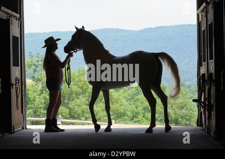 Frau und Pferd Silhouette in offenen Scheunentor, ein Landmädchen, Cowboy-Hut, Hose und Stiefel tragen. Stockfoto