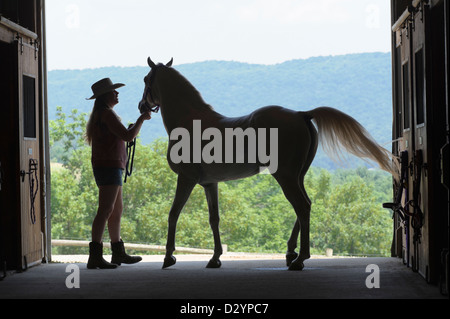 Frau und Pferd Silhouette in offenen Scheunentor, ein Landmädchen, Cowboy-Hut, Hose und Stiefel tragen. Stockfoto