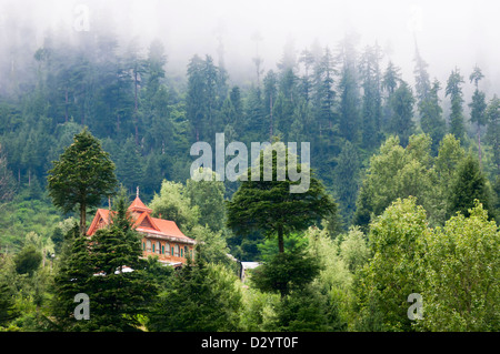 Haus in hohe Berge bedeckt durch Nadelwald und Wolken, Nord-Indien Stockfoto