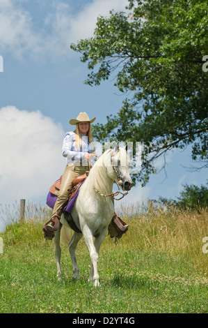 Frau Reiten auf schönen weißen Pferd draußen in der Natur und Sonnenschein, ein Cowgirl in amerikanischen westlichen Stil Kleidung. Stockfoto