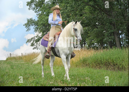 Frau Reiten auf schönen weißen Pferd draußen in der Natur und Sonnenschein, ein Cowgirl in amerikanischen westlichen Stil Kleidung. Stockfoto