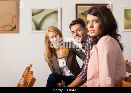 Nahaufnahme von drei attraktiven jungen Menschen lächelnd und sitzen auf Stühlen mit gerahmten abstrakte Fotografie arbeiten auf ba Stockfoto