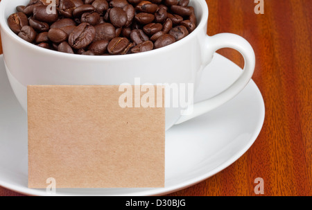 Weiße Tasse Kaffee Bohnen mit Karte für Text auf Holztisch Stockfoto