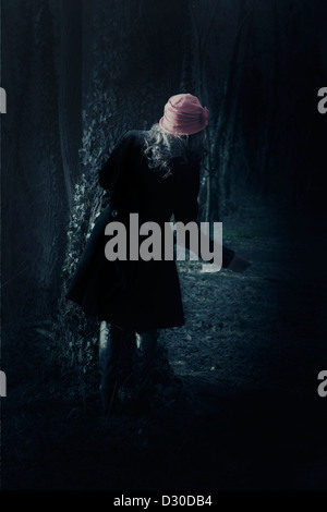 eine Frau mit einem schwarzen Mantel steht hinter einem Baum Stockfoto