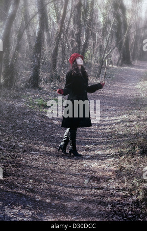 eine Frau in einem schwarzen Mantel mit roten Hut steht im Wald Stockfoto