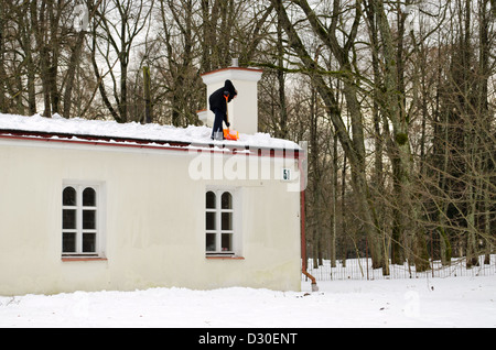 Mann in schwarz mit orange Kunststoff Schaufel Werkzeug sauber Schnee vom Dach im Winter. Stockfoto